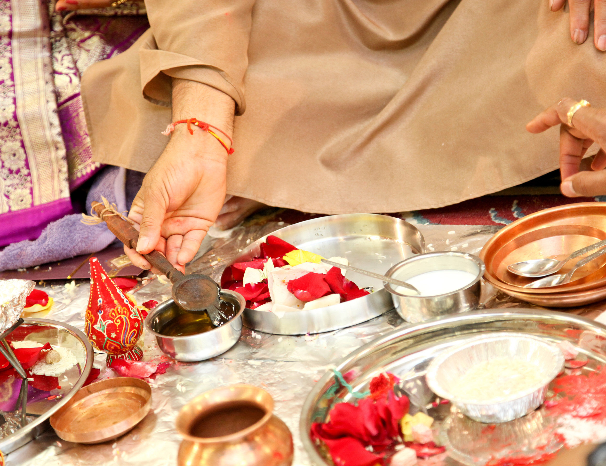 Close-up of traditional Indian wedding puja setup with priest performing rituals using ghee, flowers, and sacred items